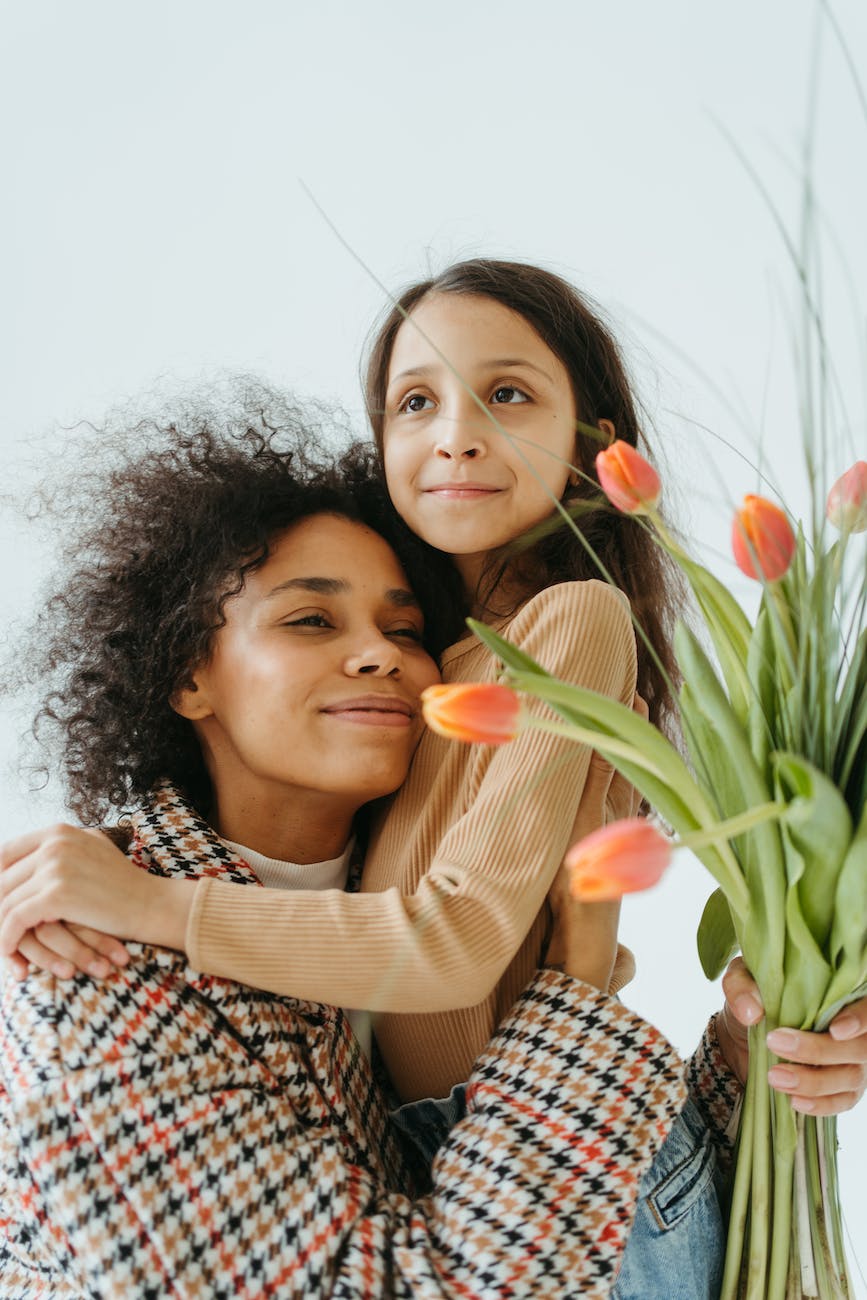 Photo by Anastasia  Shuraeva on <a href="https://www.pexels.com/photo/woman-in-checked-coat-hugging-a-child-while-holding-a-bunch-of-flowers-7173479/" rel="nofollow">Pexels.com</a>